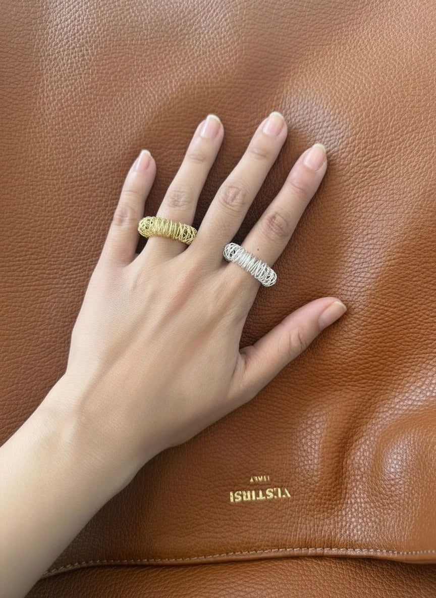 Hand wearing two rings on a brown leather surface with 'VESTIRSI' branding.